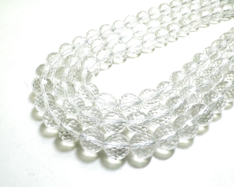 May include: Clear, faceted crystal beads strung together, forming multiple strands. The beads are round with a textured surface, reflecting light. The image shows a close-up of the beads, highlighting their transparency and intricate design. These beads are suitable for jewelry making.