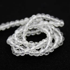 May include: A strand of clear, faceted beads, likely gemstones, is coiled on a black surface. The beads are small and round, reflecting light, suggesting a delicate jewelry item. The overall aesthetic is simple and elegant.