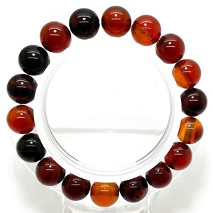 May include: A bracelet made of carnelian beads in shades of red, orange, and brown. The beads are round and have a smooth, polished finish.