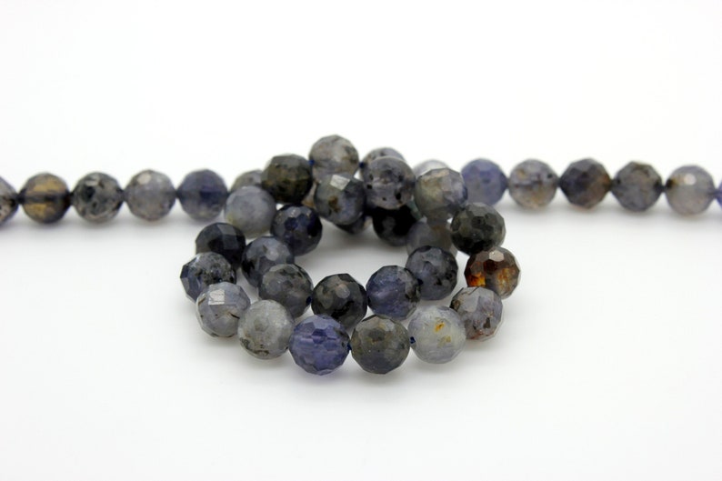 May include: A strand of faceted gemstone beads in shades of gray, blue, and brown. The beads are round and have a slightly irregular shape.
