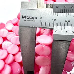 May include: Close-up of pink, oval-shaped beads. A Mitutoyo caliper, made in Japan, measures the beads. The beads are strung together, and the caliper shows a measurement of approximately 0.3 inches.
