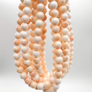 May include: A multi-strand necklace composed of smooth, round, pale peach and cream-coloured beads. The beads are arranged in several vertical loops, creating a layered effect with a consistent spherical shape and a soft, matte finish throughout.