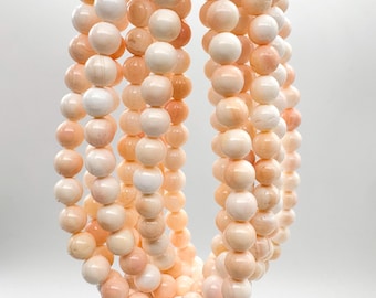 May include: A multi-strand necklace composed of smooth, round, pale peach and cream-colored beads. The beads are arranged in several vertical loops, creating a layered effect with a consistent spherical shape and a soft, matte finish throughout.