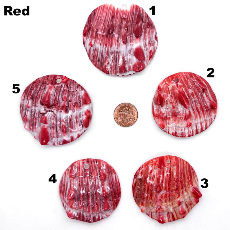 May include: Five red and white shell pendants with a hole for stringing. The pendants are round and have a textured surface. A penny is included for size comparison. The word "Red" is in the upper left corner.