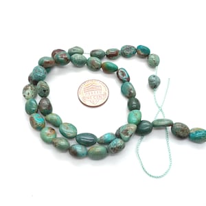 May include: Strand of turquoise-colored gemstone beads with a mix of blue, green, and brown hues. The beads are oval-shaped and strung on a light green cord. A US one-cent coin is next to the beads for size comparison.