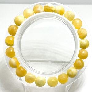 May include: A bracelet made of yellow amber beads. The beads are round and have a smooth, polished finish. The bracelet is strung on a clear elastic cord.