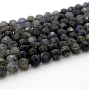 May include: A strand of faceted dark blue and gray gemstone beads. The beads are round and have a slightly irregular shape.