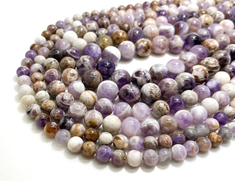 May include: A strand of round, purple, white, and brown amethyst beads. The beads are smooth and have a natural, polished finish. The beads are arranged in a circular pattern, with the largest beads in the center and the smallest beads on the outside.