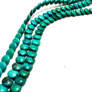 May include: Three strands of turquoise beads, each featuring a flattened, circular coin shape. The beads display a vibrant teal-green color with natural dark brown matrix veining throughout, creating a textured appearance across the strands.