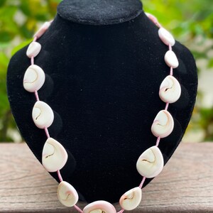 Puede incluir: Un collar de conchas rosa y blanco con forma de l&aacute;grima. El collar est&aacute; hecho de conchas naturales y est&aacute; enhebrado en un cord&oacute;n rosa.