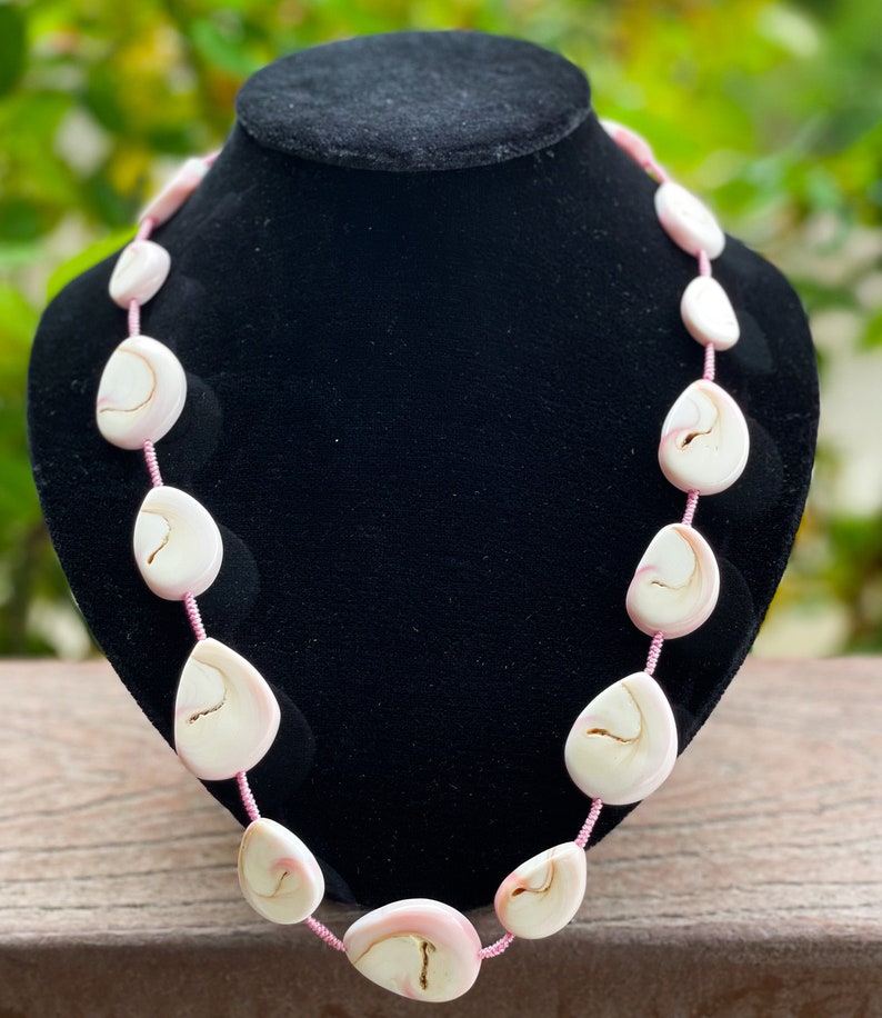 Puede incluir: Un collar de conchas rosa y blanco con forma de l&aacute;grima. El collar est&aacute; hecho de conchas naturales y est&aacute; enhebrado en un cord&oacute;n rosa.