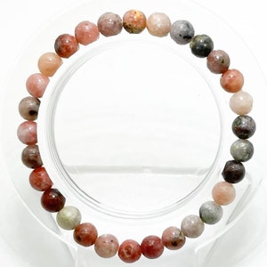 May include: A bracelet made of pink, red, and brown gemstone beads. The beads are round and have a smooth, polished finish.