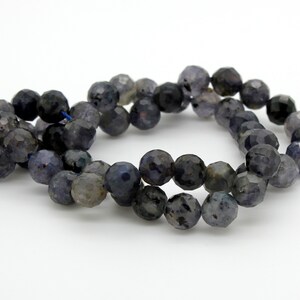 May include: A strand of dark blue faceted gemstone beads. The beads are round and have a slightly irregular shape. The beads are strung on a thin thread.