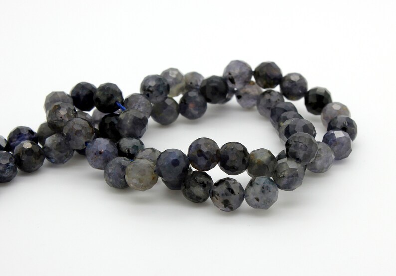 May include: A strand of dark blue faceted gemstone beads. The beads are round and have a slightly irregular shape. The beads are strung on a thin thread.