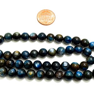 May include: A strand of blue and gold tiger's eye beads. The beads are round and smooth, and they have a shimmering effect. The beads are strung on a blue cord.
