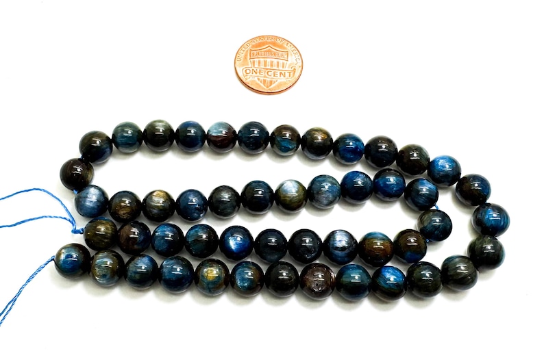 May include: A strand of blue and gold tiger's eye beads. The beads are round and smooth, and they have a shimmering effect. The beads are strung on a blue cord.