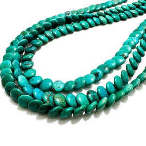 May include: Strands of turquoise gemstone beads in varying shades of teal and turquoise. The beads are oval-shaped and strung together, creating a layered effect. The beads are displayed against a white background.