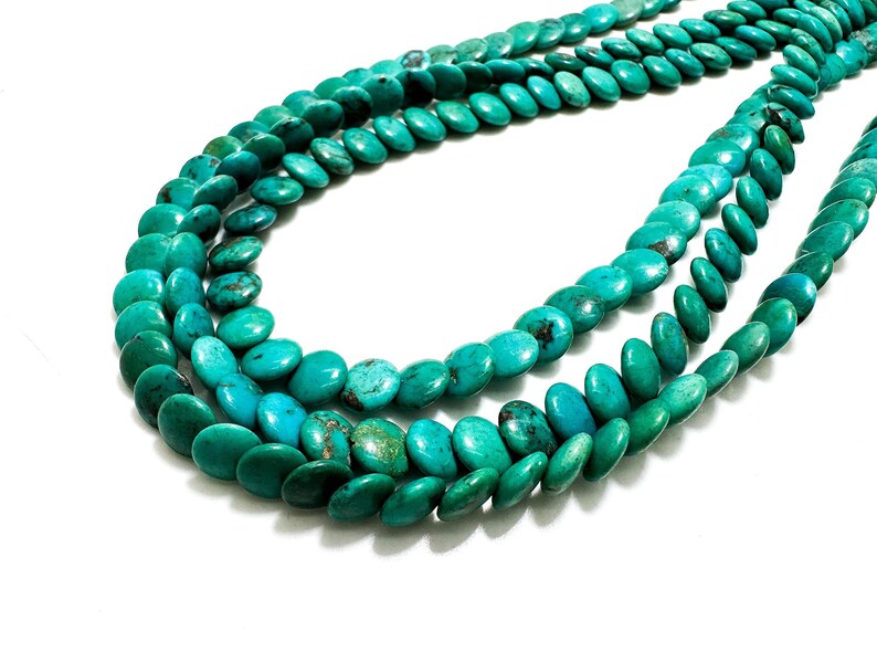 May include: Strands of turquoise gemstone beads in varying shades of teal and turquoise. The beads are oval-shaped and strung together, creating a layered effect. The beads are displayed against a white background.