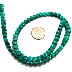 May include: A strand of round, flat turquoise beads with natural dark matrix veining, arranged in a loose loop. A copper-colored United States one-cent coin is placed in the center for scale, measuring approximately 0.75 inches in diameter.