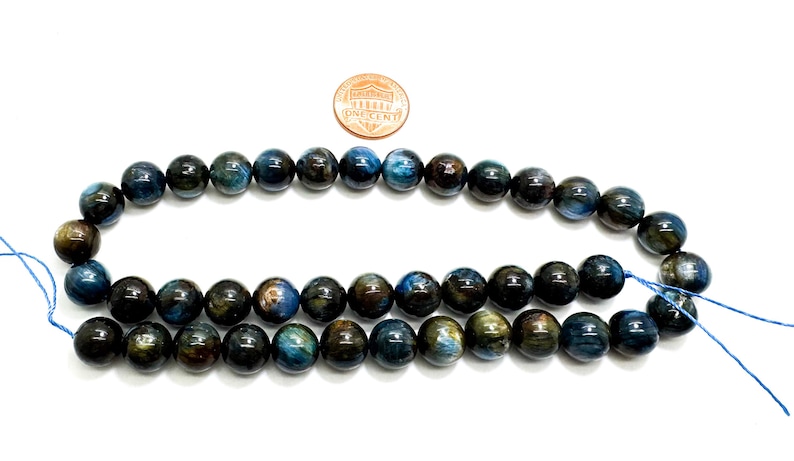 May include: A strand of blue tiger's eye beads, approximately 8mm in diameter. The beads have a dark blue base with golden brown streaks and a slight shimmer.