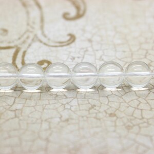 May include: A strand of clear glass beads, strung together on a white thread. The beads are round and smooth, and they reflect the light beautifully.