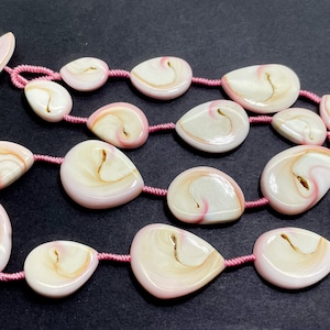 Puede incluir: Una hebra de cuentas de concha rosa y blanca con un cord&oacute;n rosa. Las cuentas tienen forma de l&aacute;grima y tienen un patr&oacute;n de remolino.