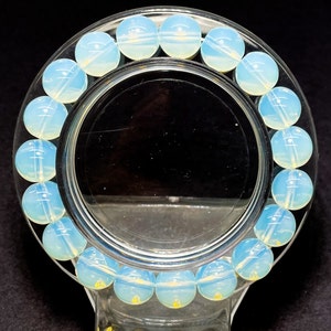 May include: A bracelet made of light blue opal beads. The beads are round and smooth, and they are strung together on a clear elastic cord.
