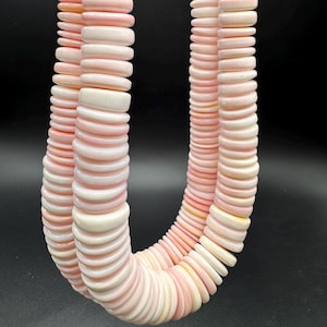 May include: A double-strand necklace composed of numerous smooth, flat, disc-shaped beads in varying shades of pale pink and cream. The beads are strung together in a continuous loop, creating a uniform, rounded texture throughout the entire piece.
