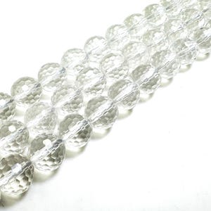 May include: Strands of clear, faceted crystal beads. The beads are round with a textured surface, strung together on a clear cord. The beads are displayed against a white background, creating a bright and clean aesthetic.