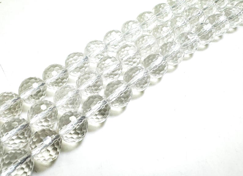 May include: Strands of clear, faceted crystal beads. The beads are round with a textured surface, strung together on a clear cord. The beads are displayed against a white background, creating a bright and clean aesthetic.