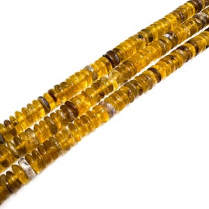 May include: Close-up of three strands of amber-colored gemstone beads. The beads are small, round, and have a slightly irregular shape. The color varies from a light yellow to a deeper, richer amber. The beads are strung together, creating a textured and visually appealing pattern.