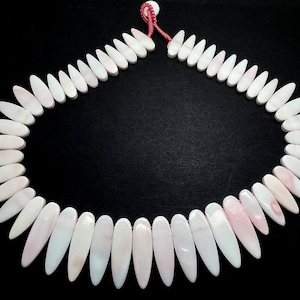 May include: A necklace made of white and pink shell beads in a teardrop shape. The beads are strung on a red cord.