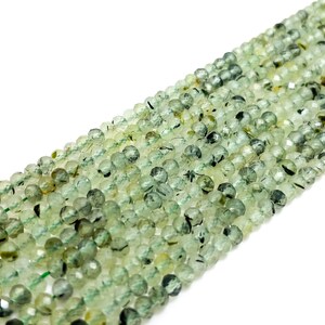 May include: A strand of green and black gemstone beads. The beads are round and have a faceted finish.