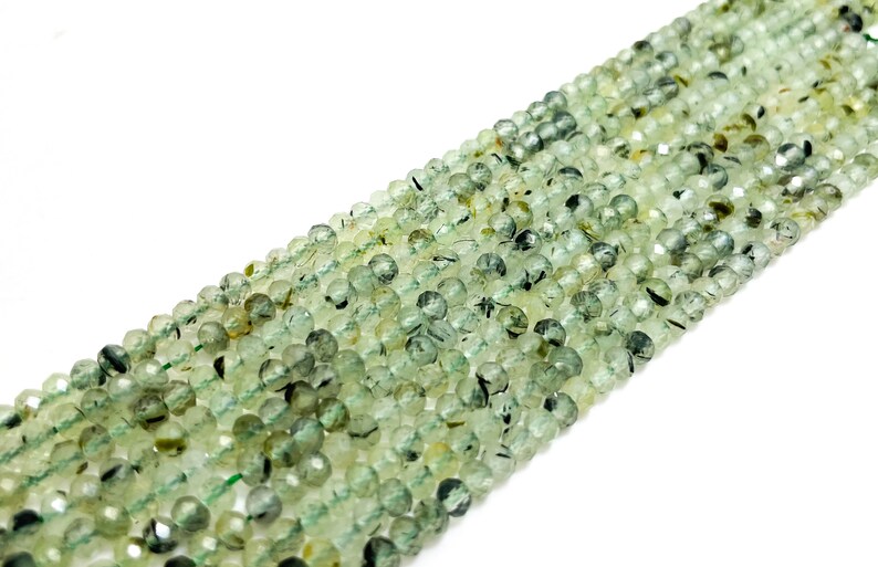 May include: A strand of green and black gemstone beads. The beads are round and have a faceted finish.