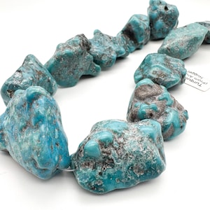 May include: A strand of raw turquoise nuggets featuring irregular shapes and varying shades of bright blue and teal with dark brown matrix inclusions. The stones are strung together on a thin wire, showcasing a natural, unpolished, and textured surface.