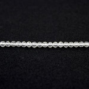 May include: A strand of small, clear, round beads. The beads are strung together, creating a delicate necklace or bracelet component. The beads are evenly spaced and appear to be made of a transparent material.
