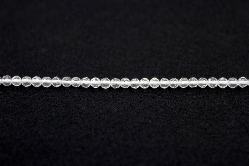 May include: A strand of small, clear, round beads. The beads are strung together, creating a delicate necklace or bracelet component. The beads are evenly spaced and appear to be made of a transparent material.