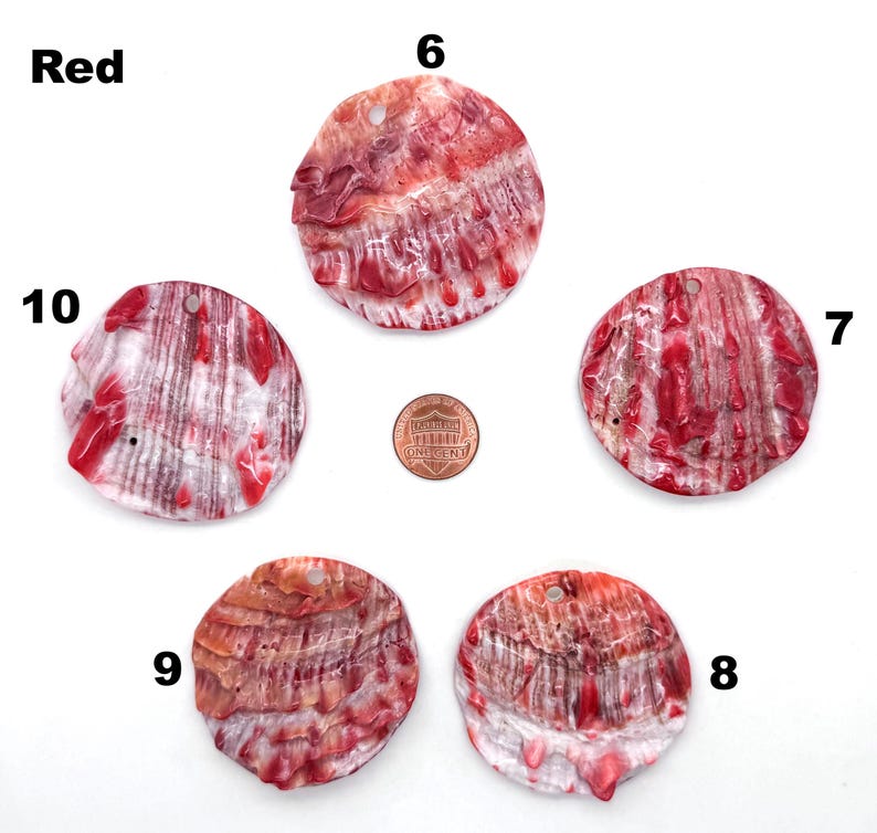 May include: Five red and white shell pendants with a hole drilled at the top for stringing. The shells have a natural, textured appearance with red streaks and patterns. A penny is included for size reference. The word "Red" is in the upper left corner.