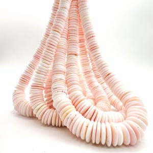 May include: A long strand of pale pink disc-shaped beads arranged in a cascading loop. The beads are uniform in size and shape, featuring a smooth, matte finish with subtle variations in color intensity across the individual circular pieces.
