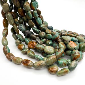 May include: A strand of polished, irregular, pebble-shaped beads in shades of teal, sage green, and earthy brown. The beads feature natural marbling and variations in color, with a smooth, glossy finish throughout the entire length of the strand.