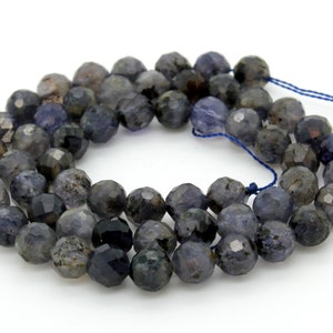 May include: A strand of dark blue faceted gemstone beads. The beads are round and have a slightly irregular shape. The beads are strung on a blue thread.