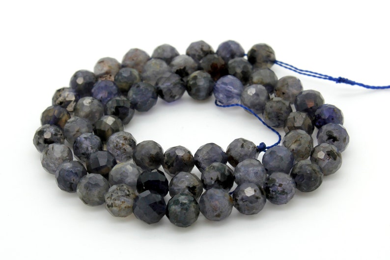 May include: A strand of dark blue faceted gemstone beads. The beads are round and have a slightly irregular shape. The beads are strung on a blue thread.