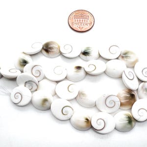 K&ouml;nnte beinhalten: Eine Kette aus wei&szlig;en Muschelkugeln mit Spiralmuster, pr&auml;sentiert auf wei&szlig;em Hintergrund. Eine Ein-Cent-M&uuml;nze liegt zur Gr&ouml;&szlig;enbestimmung &uuml;ber den Kugeln. Die Perlen haben ein nat&uuml;rliches, organisches Aussehen.