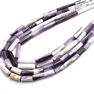 Può includere: Una collana con fili di perline tubolari viola, bianche e beige. Le perline hanno un aspetto marmorizzato, con variazioni di colore e motivo. La collana è esposta su uno sfondo bianco.