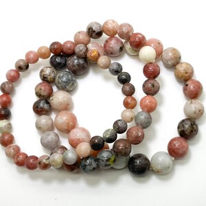 May include: Three bracelets made of pink, brown, and grey round beads. The beads have a speckled pattern.