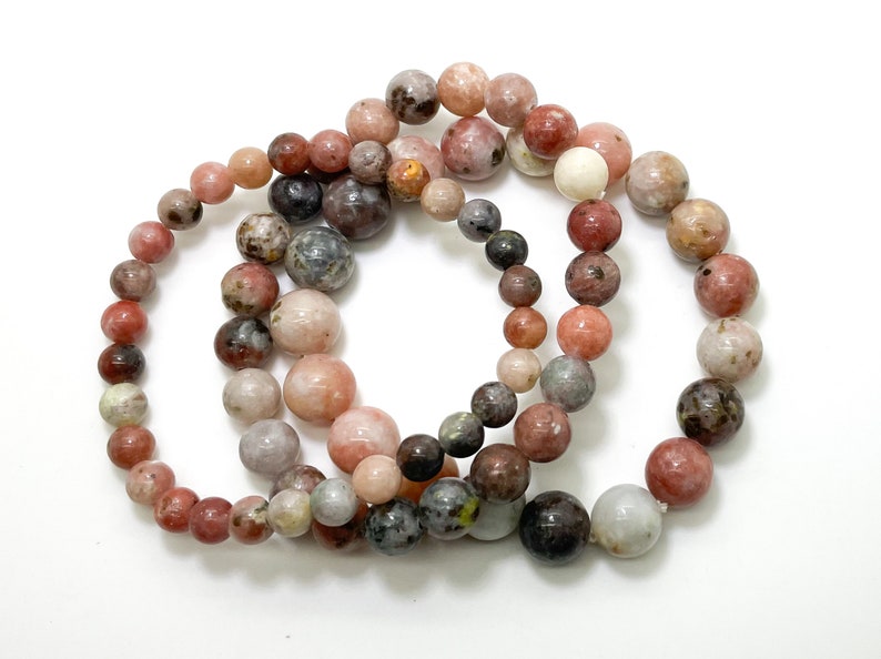 May include: Three bracelets made of pink, brown, and grey round beads. The beads have a speckled pattern.