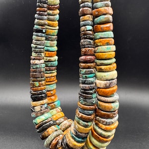 May include: A multi-strand necklace composed of numerous flat, disc-shaped beads in varying shades of turquoise, brown, tan, and black. The beads feature natural marbling and color variations, arranged in a dense, layered vertical formation.
