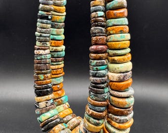 Può includere: Una collana a più fili composta da numerose perline piatte a forma di disco in varie tonalità di turchese, marrone, marrone chiaro e nero. Le perline presentano venature naturali e variazioni di colore, disposte in strati.