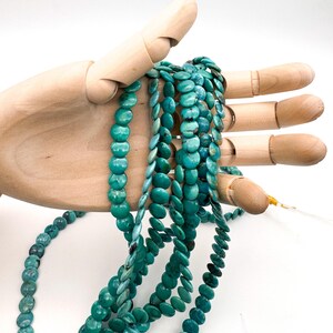 May include: Multiple strands of round, flat turquoise beads featuring natural blue-green color variations and dark matrix veining. The beads are strung on thin, clear filament, creating a collection of circular, disc-shaped gemstone components.