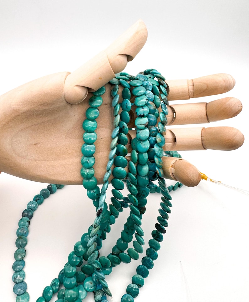 May include: Multiple strands of round, flat turquoise beads featuring natural blue-green color variations and dark matrix veining. The beads are strung on thin, clear filament, creating a collection of circular, disc-shaped gemstone components.